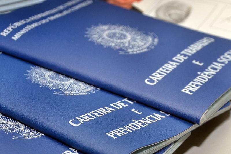 Carteiras de Trabalho e Previdência Social brasileiras, destacando as capas azuis com inscrições em branco, posicionadas sobre uma mesa em ambiente administrativo.