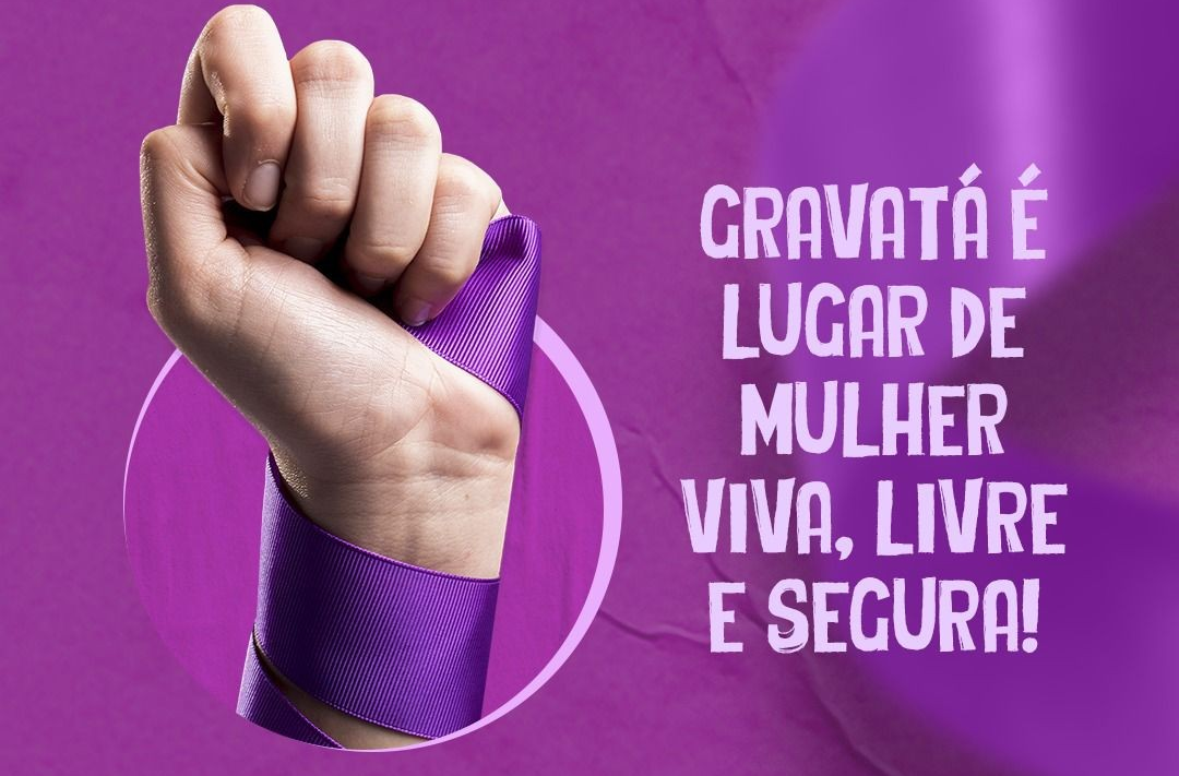 Campanha Agosto Lilás com fundo roxo, destacando uma mão feminina fechada com uma fita lilás enrolada no pulso, ao lado da frase: "Gravatá é lugar de mulher viva, livre e segura!".
