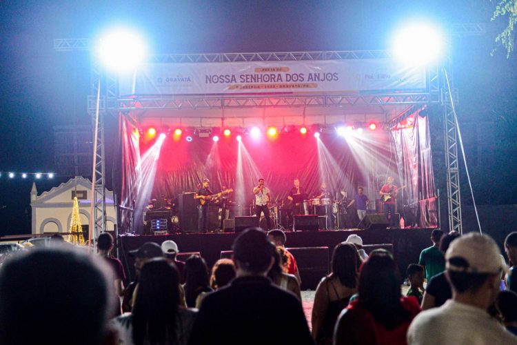 Palco iluminado durante a Festa de Nossa Senhora dos Anjos em Gravatá, com banda ao vivo se apresentando à noite diante de uma plateia.