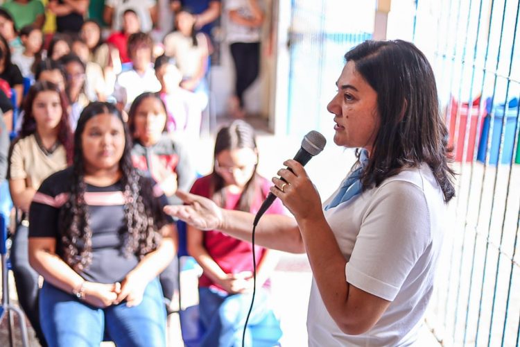Viviane Facundes fala ao microfone durante encontro com moradores em Gravatá, com público sentado ao fundo.