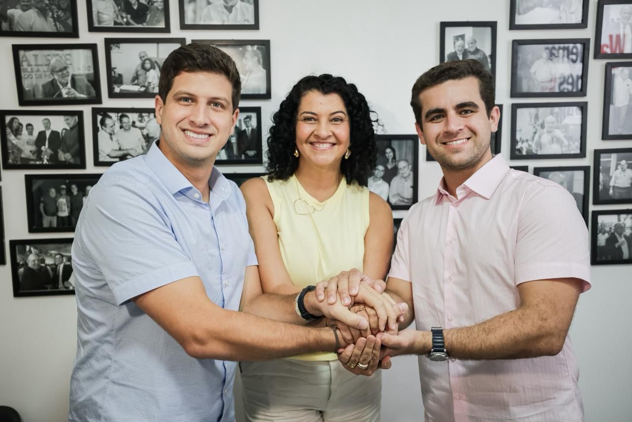 João Campos, pré-candidato ao Governo de Pernambuco; Ninha Professora, ao centro, pré-candidata à Alepe; e o advogado Wal Borges, filho do deputado estadual Waldemar Borges, aparecem juntos, com as mãos sobrepostas em um gesto de união, diante de uma parede repleta de fotos.